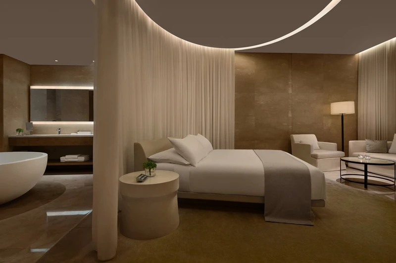 Luxury hotel suite with white bed, curved sheer curtains, freestanding bathtub and warm ambient lighting