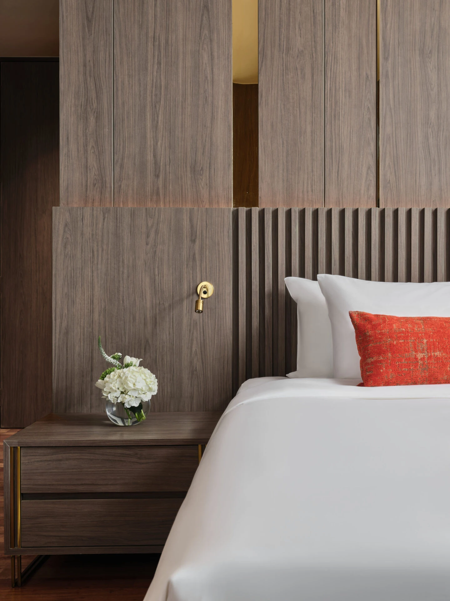 Bedside detail with brass sconce, hydrangeas and walnut slatted headboard